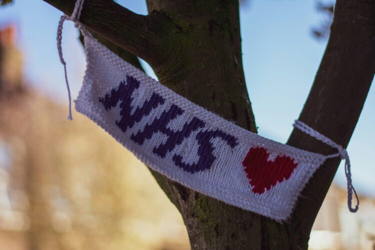 Hand knitted NHS ♥️ flag hangs on a tree, from Ruth Herring, a knitwear designer in Colliers Wood, London. Photograph by Tugce Gungormezler