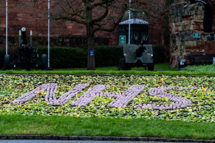 Purple flowers on grass, spelling out 'NHS'. Photograph by Samuel Goodwin